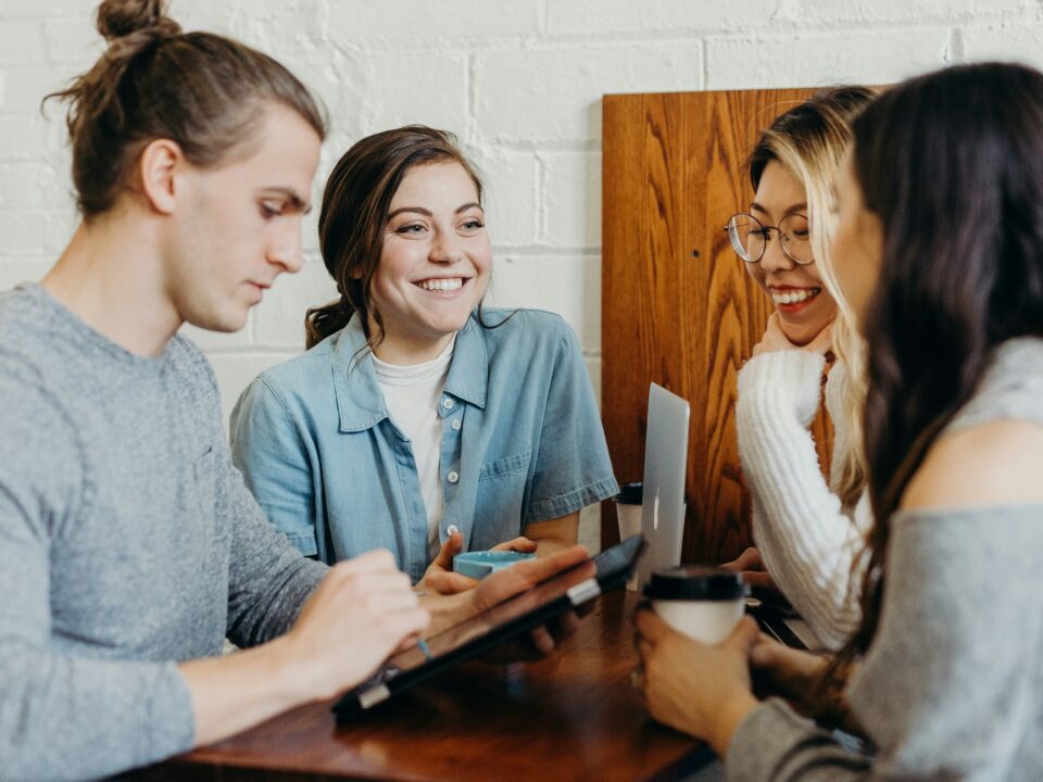 Menschen sitzen an einem Tisch und Netzwerken einfach zusammen. Sie freuen sich, weil sie sehen, wie einfach Networking sein kann.